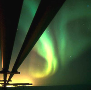 Photograph of Alaskan pipeline with aurora borealis in the background